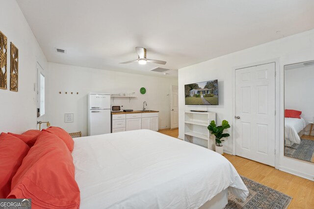 bedroom with ceiling fan, sink, white refrigerator, and light wood-type flooring