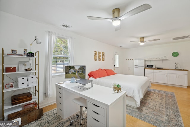 bedroom featuring ceiling fan, sink, white refrigerator, and light wood-type flooring