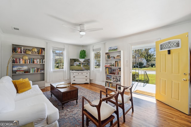 living area with ceiling fan, plenty of natural light, hardwood / wood-style floors, and ornamental molding