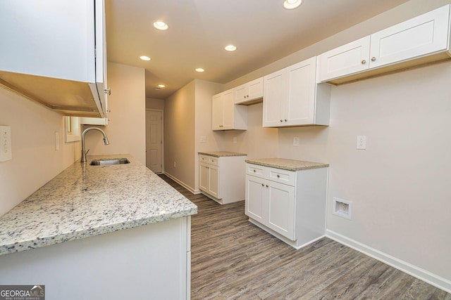 kitchen with wood finished floors, light stone counters, a sink, and recessed lighting