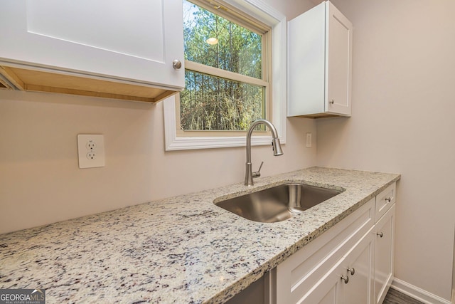 kitchen featuring light stone counters, white cabinets, and a sink