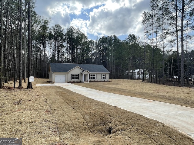 ranch-style home featuring an attached garage, a front yard, a view of trees, and concrete driveway