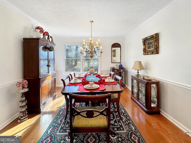 dining area featuring light wood-type flooring, a chandelier, crown molding, and a textured ceiling