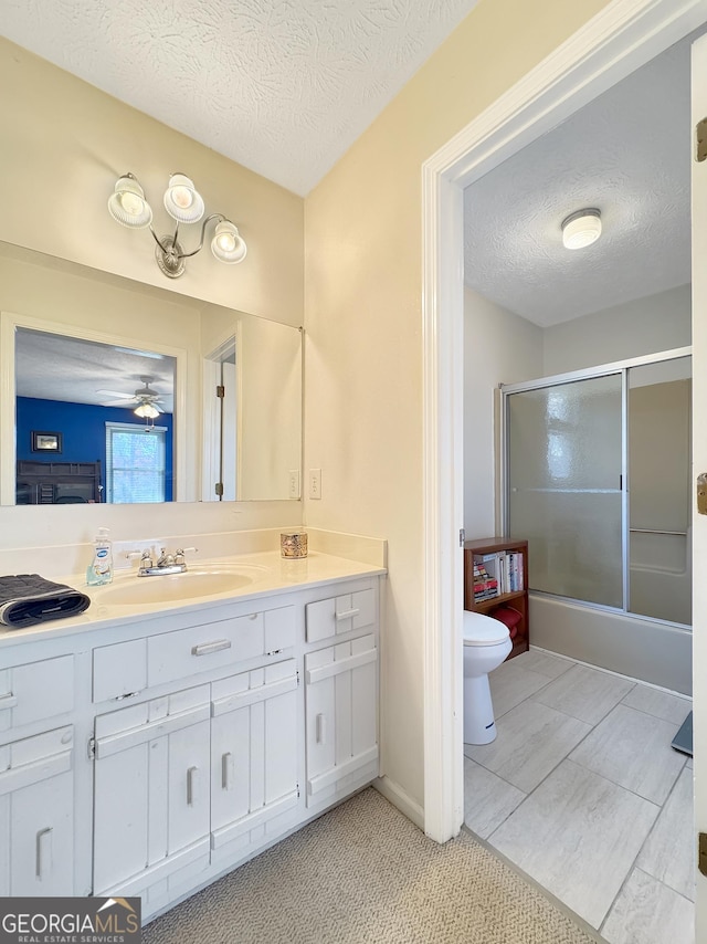 full bathroom with toilet, a textured ceiling, ceiling fan, combined bath / shower with glass door, and vanity