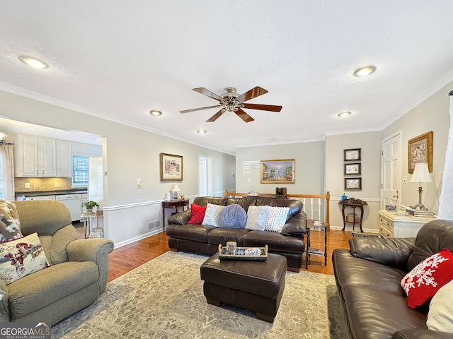 living room with ceiling fan, a textured ceiling, wood-type flooring, and ornamental molding