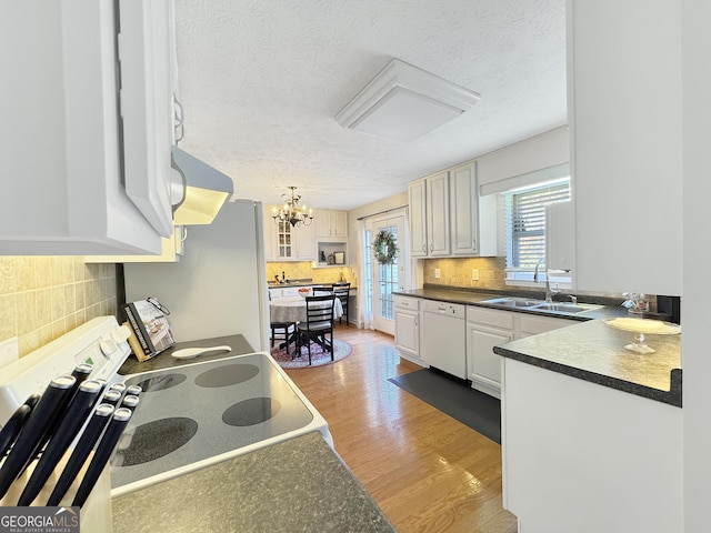 kitchen featuring range, ventilation hood, sink, white dishwasher, and white cabinets