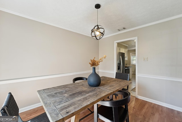 dining room featuring visible vents, baseboards, wood finished floors, and ornamental molding