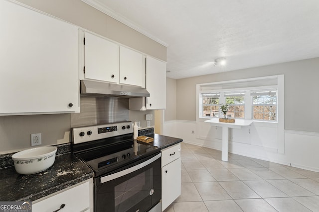 kitchen with under cabinet range hood, wainscoting, stainless steel range with electric stovetop, light tile patterned flooring, and white cabinetry