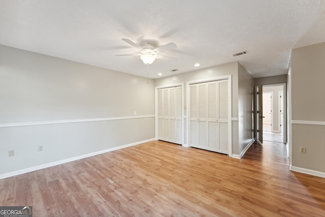 unfurnished bedroom featuring visible vents, baseboards, a textured ceiling, light wood-type flooring, and two closets