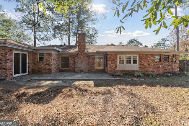 rear view of house featuring brick siding, a chimney, and a patio area