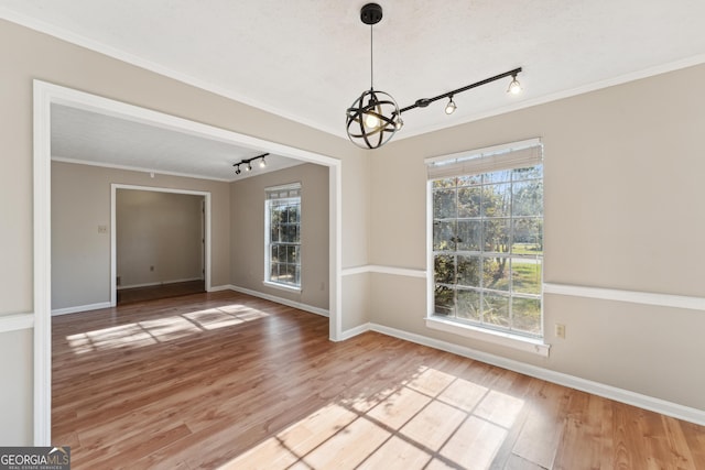 unfurnished dining area with wood-type flooring, plenty of natural light, ornamental molding, and an inviting chandelier