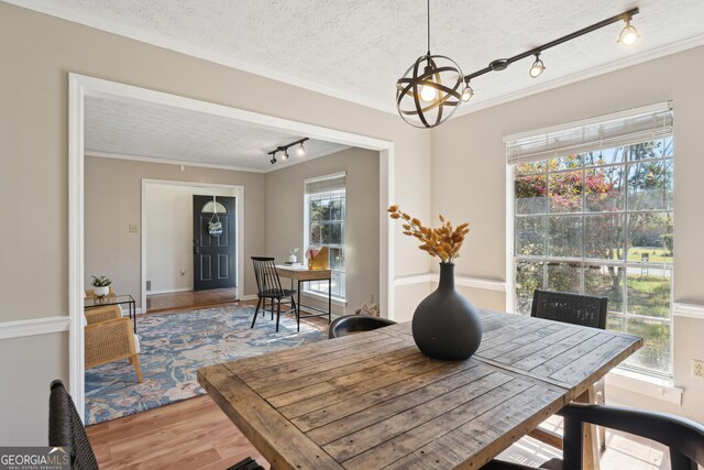 unfurnished dining area with an inviting chandelier, track lighting, crown molding, and hardwood / wood-style floors