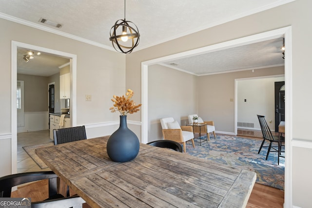 dining room featuring light wood finished floors, visible vents, a textured ceiling, and ornamental molding