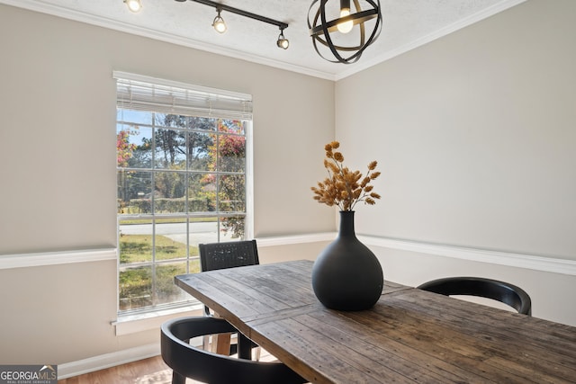 dining area featuring track lighting, a textured ceiling, wood finished floors, crown molding, and baseboards