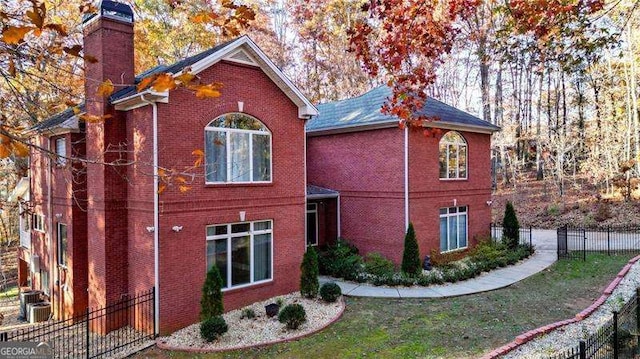 view of side of property with a lawn, a chimney, fence, cooling unit, and brick siding