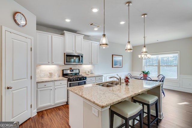 kitchen featuring white cabinetry, stainless steel appliances, pendant lighting, a center island with sink, and light wood-type flooring