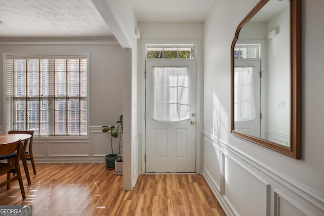 entryway featuring light hardwood / wood-style flooring, a textured ceiling, and ornamental molding