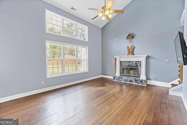 unfurnished living room featuring hardwood / wood-style flooring, ceiling fan, high vaulted ceiling, and a high end fireplace