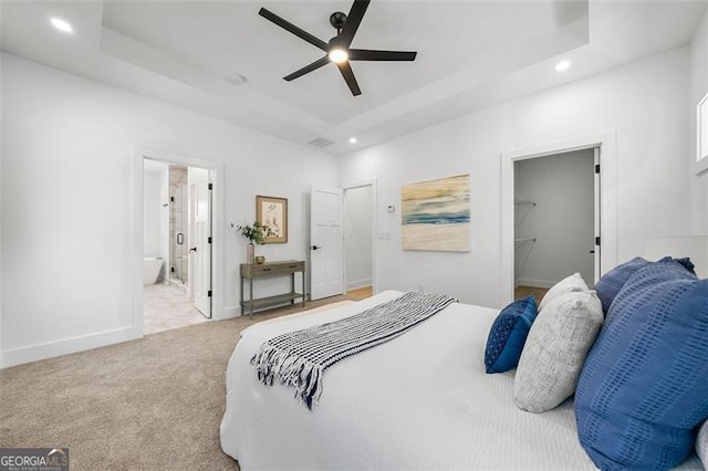 bedroom featuring ensuite bath, a spacious closet, ceiling fan, a tray ceiling, and light carpet