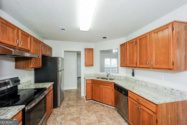 kitchen with sink, light stone counters, a textured ceiling, light tile patterned floors, and appliances with stainless steel finishes