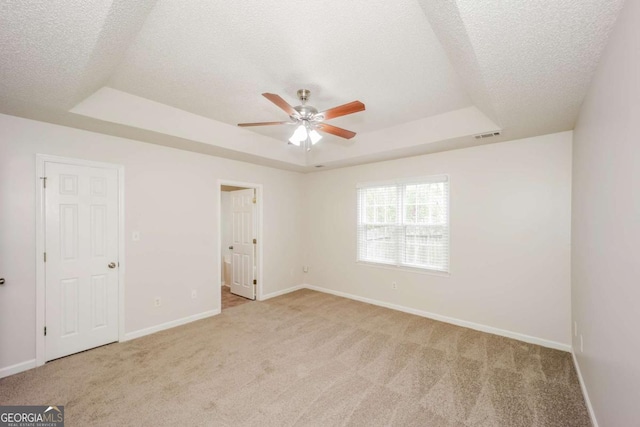 unfurnished bedroom featuring a textured ceiling, light colored carpet, a raised ceiling, and ceiling fan