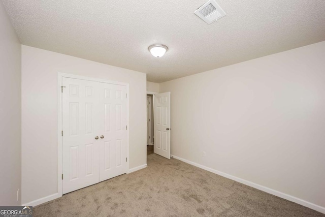 unfurnished bedroom featuring a textured ceiling, light carpet, and a closet