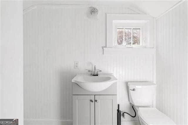 bathroom with wooden walls, vanity, lofted ceiling, and toilet