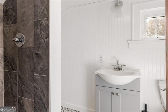 bathroom featuring a tile shower, vanity, and toilet