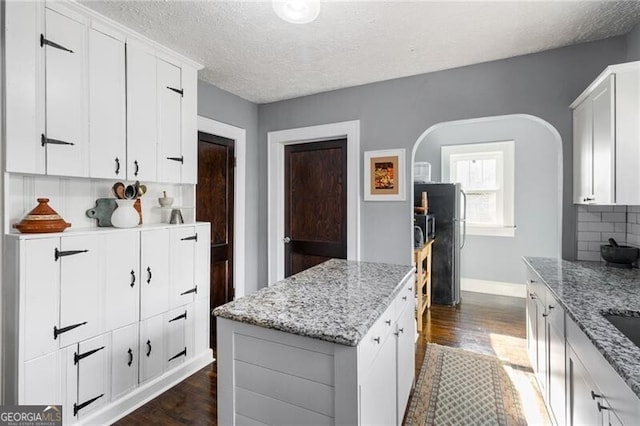 kitchen featuring white cabinets, dark hardwood / wood-style floors, a textured ceiling, tasteful backsplash, and light stone counters