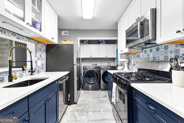 kitchen featuring blue cabinets, sink, washer and dryer, a textured ceiling, and appliances with stainless steel finishes