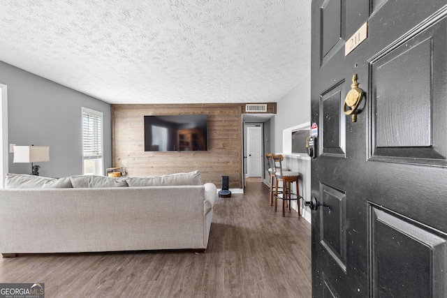 living room with a textured ceiling, dark hardwood / wood-style flooring, and wood walls