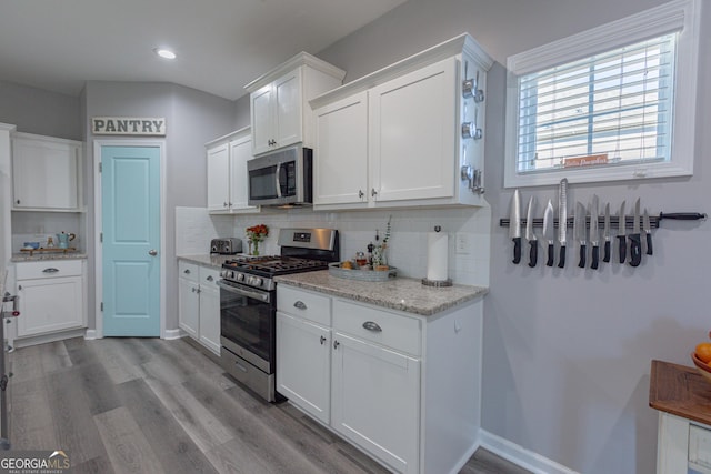 kitchen with white cabinets, decorative backsplash, light wood-type flooring, light stone counters, and stainless steel appliances