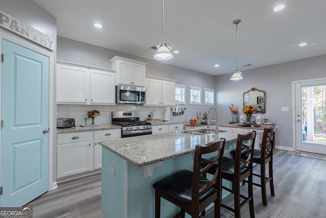 kitchen featuring a kitchen island with sink, white cabinets, sink, appliances with stainless steel finishes, and decorative light fixtures