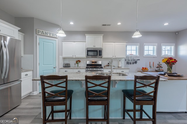 kitchen featuring pendant lighting, white cabinetry, stainless steel appliances, and an island with sink