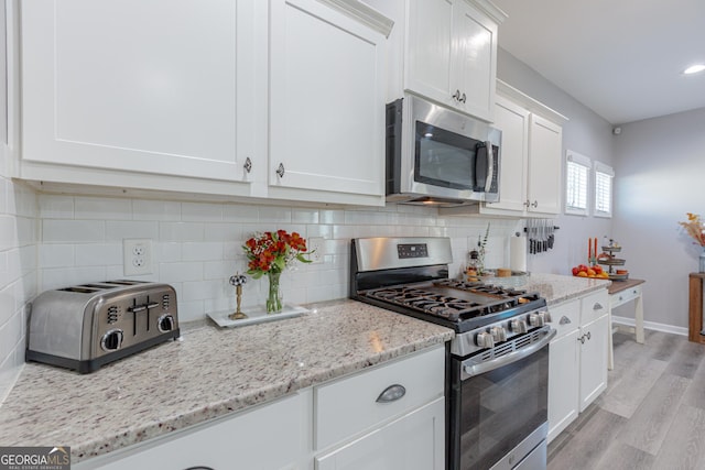 kitchen featuring white cabinets, light hardwood / wood-style flooring, decorative backsplash, light stone countertops, and stainless steel appliances