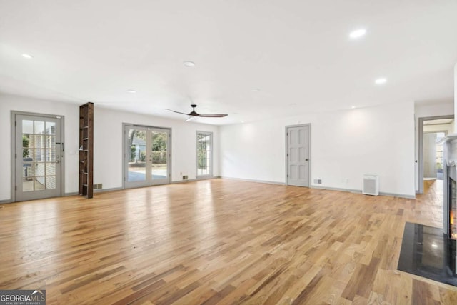 unfurnished living room featuring french doors, a healthy amount of sunlight, ceiling fan, and light hardwood / wood-style flooring