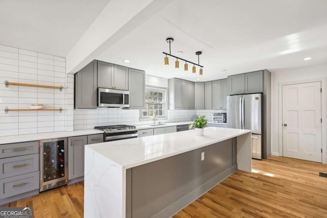 kitchen featuring wine cooler, decorative light fixtures, a center island, light hardwood / wood-style flooring, and appliances with stainless steel finishes