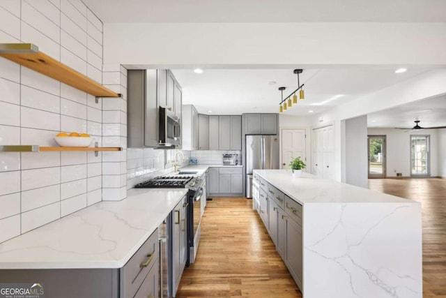 kitchen with hanging light fixtures, decorative backsplash, light stone countertops, and appliances with stainless steel finishes