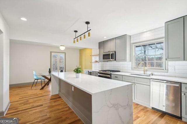 kitchen featuring a kitchen island, appliances with stainless steel finishes, sink, hanging light fixtures, and light stone countertops