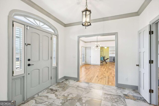 foyer entrance with crown molding, light wood-type flooring, and a notable chandelier