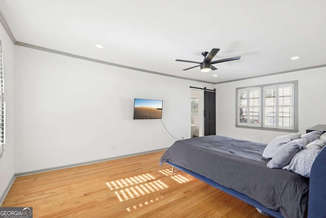 bedroom featuring ceiling fan, ornamental molding, a barn door, and wood-type flooring