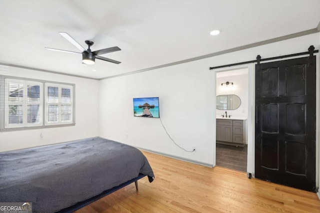 bedroom featuring crown molding, ceiling fan, connected bathroom, a barn door, and light wood-type flooring