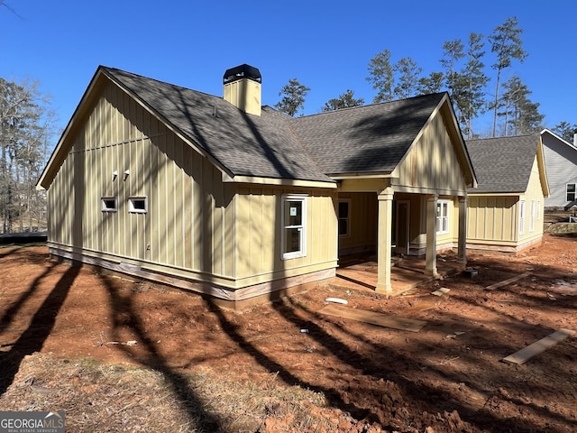 rear view of property featuring a patio area, roof with shingles, and a chimney