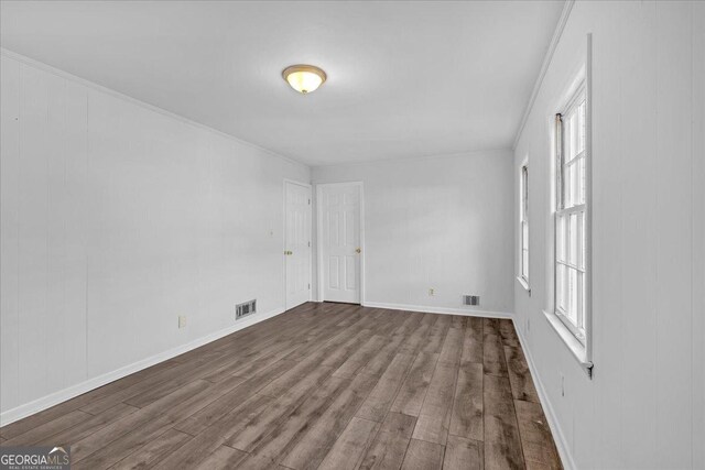 empty room with hardwood / wood-style flooring, plenty of natural light, and crown molding