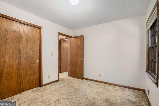 unfurnished bedroom featuring a textured ceiling, light carpet, and a closet