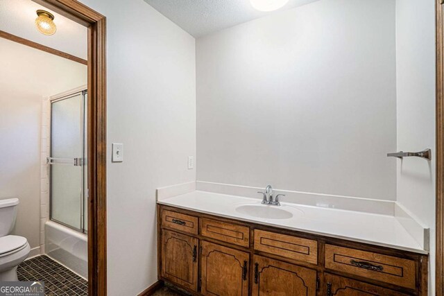 full bathroom featuring combined bath / shower with glass door, vanity, a textured ceiling, tile patterned flooring, and toilet