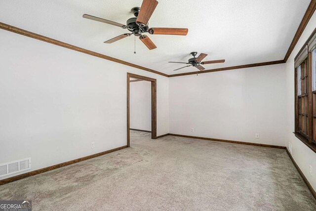 empty room with a textured ceiling, ceiling fan, crown molding, and light carpet