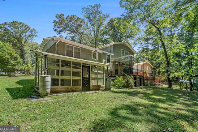 rear view of house with a lawn, a sunroom, and a deck