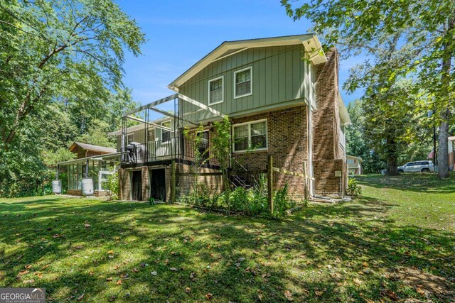 back of property featuring a yard, a deck, and a sunroom