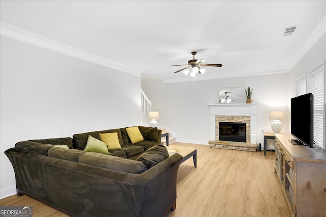 living room with ceiling fan, a fireplace, crown molding, and light wood-type flooring